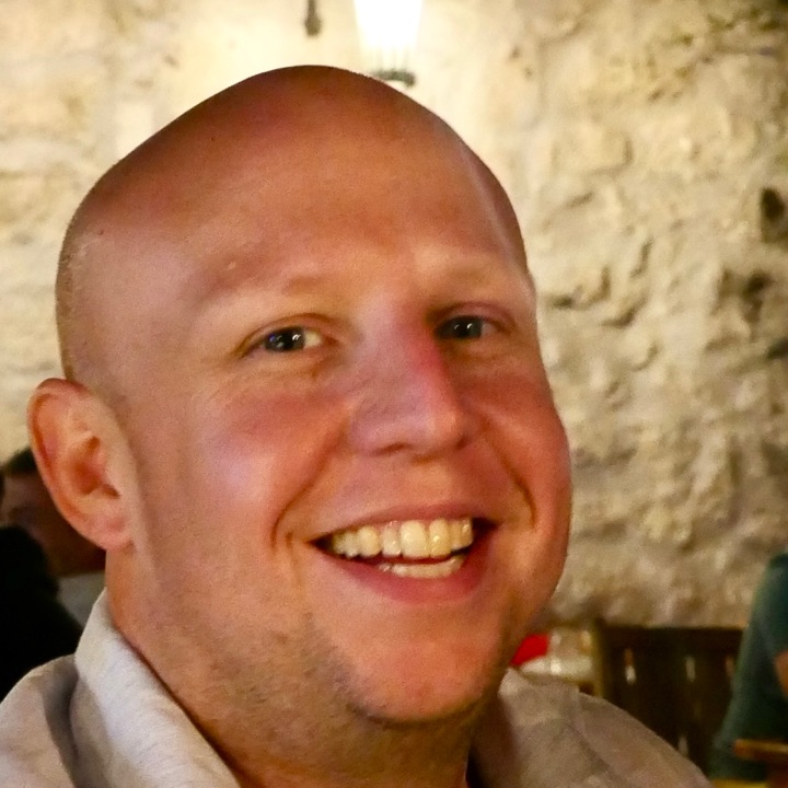 Ryan Collins, smiling, at dinner in front of a whitewashed stone wall.